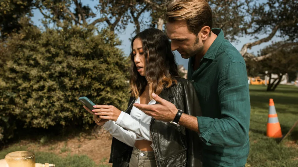 A man looks over the shoulder of a woman who is looking at her phone