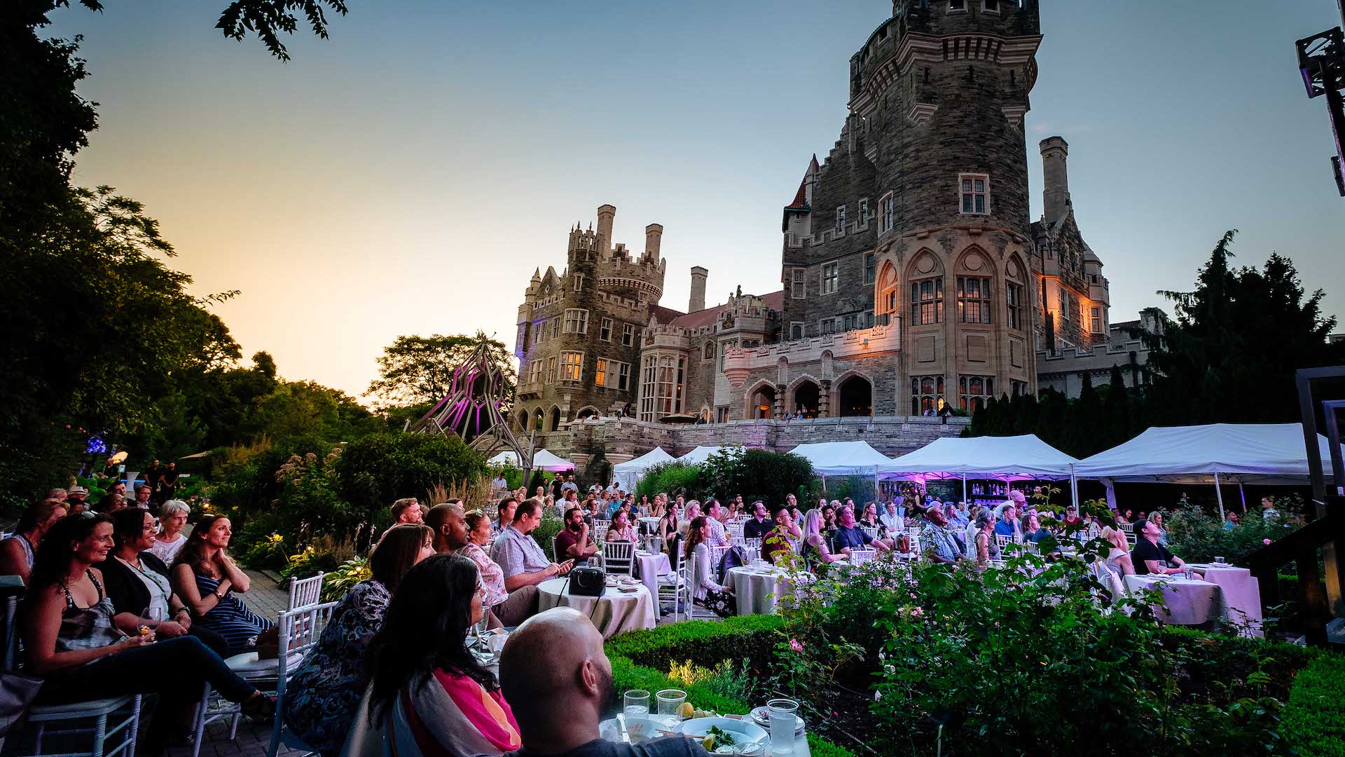 A group of people sit in the gardens of Casa Loma at sunset