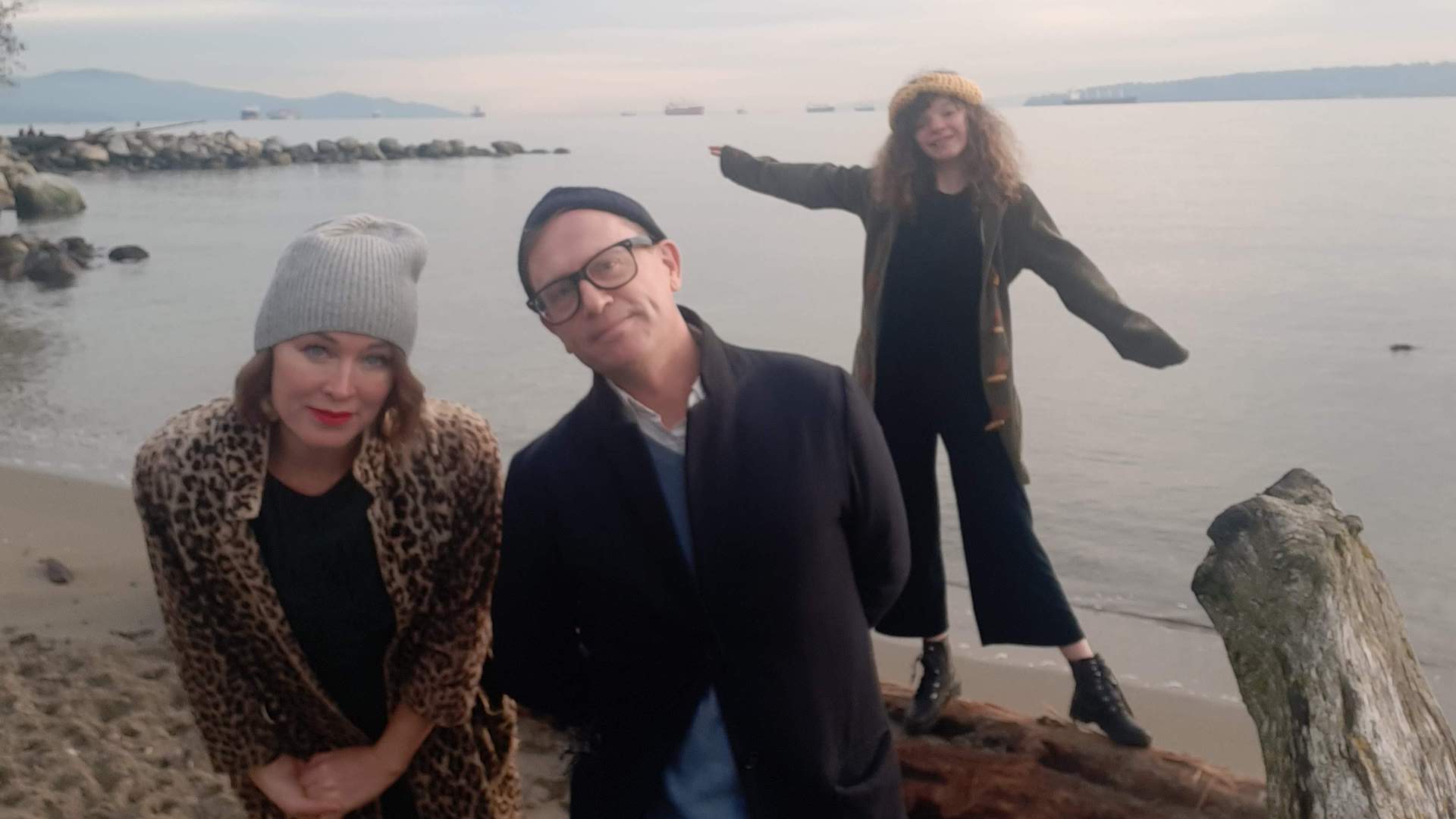 Moya O'Connell, Torquil Campbell and their child Ellington stand on a beach in front of the water